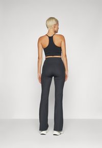 Top court en maille noire associé à un pantalon noir évasé taille haute, présentant un tissu texturé et une silhouette ajustée.