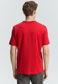 Camiseta de algodón roja con mangas cortas, escote redondeado, textura suave y un diseño sencillo, vista desde la parte posterior.
