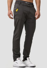 Pantalones gris con corte cónico, fabricados con una suave mezcla de algodón, que presentan un diseño texturizado, múltiples bolsillos y una etiqueta de marca visible en la cintura.