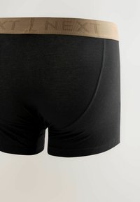 Boxer shorts neri realizzati in un tessuto morbido, caratterizzati da un elastico beige in vita con il logo "NEXT" stampato. Texture liscia e design aderente.