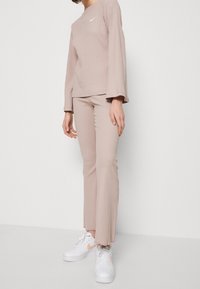 Beige ribbat långärmad topp med utsvängda ärmar och matchande ribbade byxor. Vita sneakers med en rosa accent kompletterar outfiten.