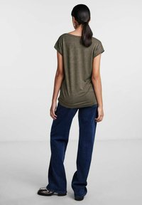 Olive green short-sleeve top with a relaxed fit, paired with loose dark blue denim trousers and black platform shoes. Smooth texture.