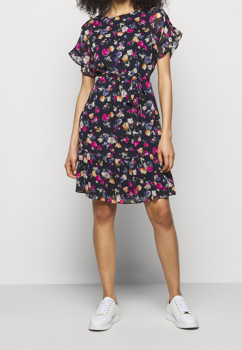 Kwiatowa sukienka w kolorze granatowym z krótkimi falbaniastymi rękawami, paskiem w talii i warstwowym dołem; ozdobiona kolorowym nadrukiem kwiatów, wykonana z lekkiego materiału.