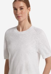Vit kortärmad stickad tröja med rund halsringning, med en mjuk textur och subtilt mönster vid axelsömmarna.