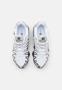 Hvite mesh sneakers med sorte detaljer, med en rund tå, tykk svart såle og forsterket snøresystem. Prentet logo på tungen.