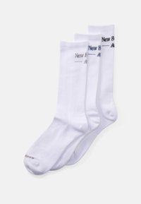 Three pairs of white crew socks with ribbed cuffs and "New Balance" branding in black, gray, and navy blue on the top side.