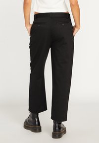 Pantalon noir à jambes larges en coton, avec poches arrière à boutons et taille plate. Associé à des bottes noires à lacets.