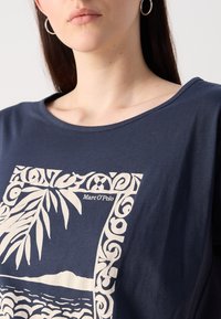 Navy blue t-shirt featuring a cream-colored graphic with a botanical pattern and the text "Marc O’Polo" in a decorative frame.