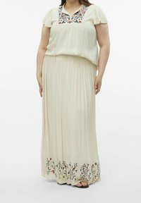 Jupe maxi plissée crème avec broderie florale au bas, assortie d'un blouse correspondante avec un col brodé et des manches courtes.