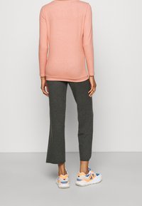 Dlouhý rukáv, světle růžový top s kulatým výstřihem, v kombinaci s tmavě šedými rozšířenými kalhotami a vícebarevnými sportovními botami.