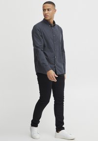Mørkeblå skjorte med krage, lange ermer og teksturert stoff, parret med svarte slim-fit bukser og hvite sneakers.