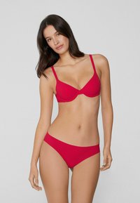 Czerwony zestaw bielizny składający się z usztywnionego biustonosza z regulowanymi ramiączkami oraz dopasowanych majtek typu bikini o niskim stanie. Gładka faktura, prosty design, bez widocznych wzorów.