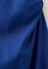 Tissu bleu à texture lisse et plis doux créant des ombres douces sur un fond clair.