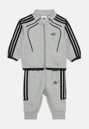 Jasnoszary dres dla malucha z czarnymi paskami na rękawach i spodniach, z przednim zamkiem błyskawicznym i logo Adidas na piersi i udzie.