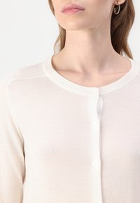 Lys beige cardigan med rund hals, knappelukking og fin strikketekstur. Ingen synlige mønstre eller detaljer.