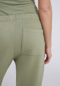 Pantalons de survêtement vert olive clair avec une texture douce, dotés d'une taille élastique et d'une poche arrière plaquée.