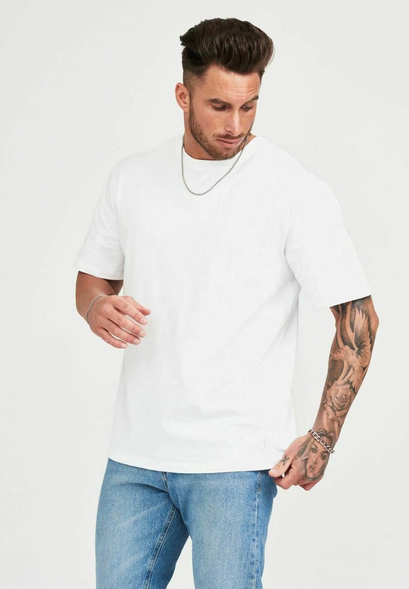 Vit bomull t-shirt med korta ärmar, avslappnad passform och rund halsringning. Bärs med ljusblå denimjeans.