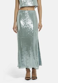 Pailletten maxi rok in licht mintgroen met een zijsplit. Kenmerkt zich door een glinsterende textuur en een getailleerd silhouet, gecombineerd met zwarte hakken.