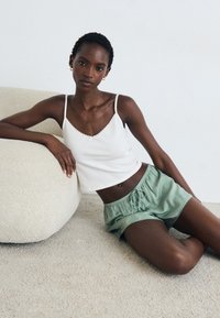 Débardeur blanc à côtes avec des bords festonnés, associé à un short en satin vert clair avec une taille élastique et un cordon de serrage.
