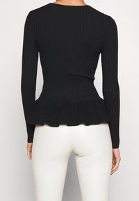 Black ribbed long-sleeve top with a peplum hem. Made of textured material, features fitted bodice and flared lower section.