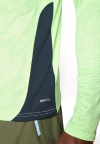 Kurzärmliges Sportshirt in Neon-Grün mit einem strukturierten Muster, das an der Seite einen dunkelblauen Akzent und das "DRYCELL"-Logo aufweist.