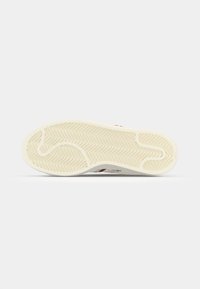 Shoe outsole featuring a beige rubber material with a herringbone pattern, curved grooves, and a smooth surface for traction.