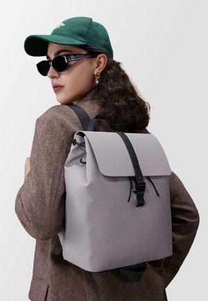 Zaino impermeabile grigio con pattina pieghevole, accessori neri e spallacci regolabili. Superficie liscia, linee pulite e design minimale.