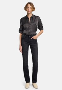 Svart knapp-up blus med rullade ärmar och en jämn textur, tillsammans med åtsittande mörka jeans och ljusa klackskor.