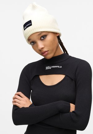 Ribbed black long-sleeve top with a high neck and cutout, featuring "KARL LAGERFELD JEANS" logo. Cream beanie with a black label accent.