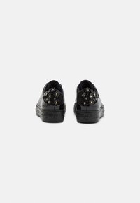 Sneaker nere con finitura in pelle liscia, caratterizzate da accenti testurizzati e decorazioni floreali sul tallone. Suole piatte, design minimalista.