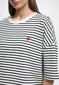 Μαύρη και λευκή ριγέ μπλούζα με στρογγυλή λαιμόκοψη, με μικρή κόκκινη κεντημένη καρδιά στο στήθος, κατασκευασμένη από βαμβακερό ύφασμα.