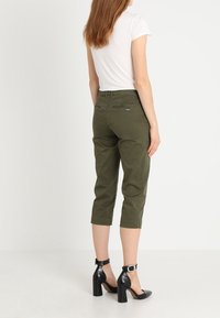 Olijfgroene cropped broeken van katoen, met een slim fit ontwerp, achterzakken en opgerolde manchetten, gecombineerd met zwarte enkelbandhakken.