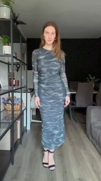 Dolga obleka s tesnim krojem v sivi barvi z valovitim vzorcem. Ima eleganten silhuet in je kombinirana s črnimi natikači na zaponko.