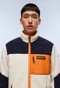 Fleece jacket with navy, cream, and orange color blocks. High collar, full front zipper, and a zippered chest pocket. Textured fabric.