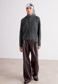 Gray wool jacket with a high collar, front button closure, and long sleeves, paired with brown faux leather wide-leg trousers.
