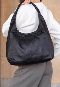 Black leather hobo bag with a braided handle, smooth texture, and soft, rounded shape. Seam detailing on front for added visual interest.