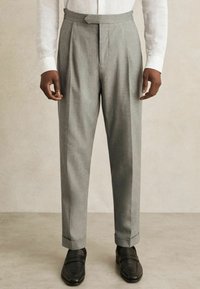 Gray pleated trousers with tailored fit, made of textured fabric. Features a hidden closure and cuffed hems, paired with black loafers.