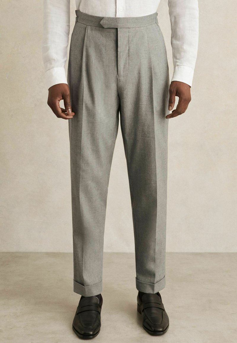 Gray pleated trousers with tailored fit, made of textured fabric. Features a hidden closure and cuffed hems, paired with black loafers.