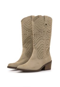Botas de cowboy de ante beige con detalles perforados, punteras en punta y tacón apilado, que presentan un lazo decorativo en el eje superior.