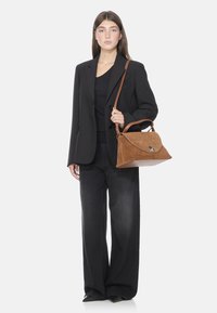 Borsa in suede tan con chiusura a pattina curva e hardware in argento. La borsa presenta una tracolla rimovibile e un design strutturato e morbido.