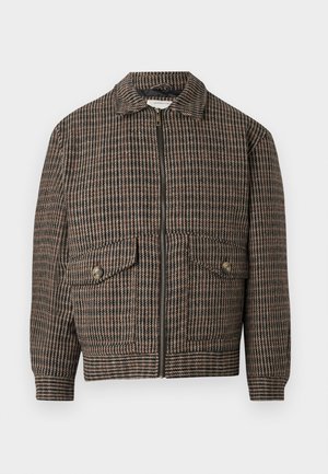 Ruskea houndstooth-kuvioinen takki, jossa on kaulus, etuvetoketju ja kaksi läpällistä taskua. Siinä on ribbireunus ja hihansuut, jotka antavat istuvan ilmeen.