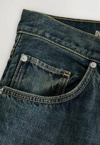 Jean en denim bleu foncé avec poche avant visible et petite poche à monnaie, présentant des surpiqûres contrastantes orange et des rivets métalliques aux coins des poches.