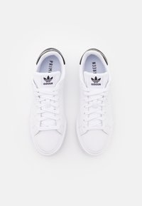 Bílé tenisky s hladkým koženým svrškem, gumovou podrážkou, černými akcenty na patě a perforovanými detaily po stranách.