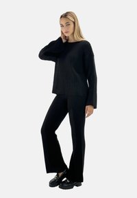Svart ribbat tvådelat set bestående av en långärmad topp med avslappnad passform och utsvängda byxor. Bärs med kraftiga svarta plattformsskor.