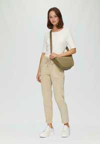 Witte ribbelige top met korte mouwen, beige corduroy tapered broek en witte platform sneakers. Groene schoudertas met een gladde textuur.