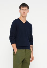 Suéter azul marinho em malha suave com punhos e bainha canelados, combinado com calças verde-oliva. Design simples e moderno.