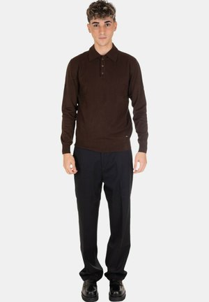 Polo shirt lungo a maniche con lavorazione a maglia color marrone, con colletto e una pattina con tre bottoni, abbinato a pantaloni e scarpe neri.