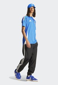 Maillot de sport bleu avec des accents blancs, présentant des manches rayées ; pantalon noir avec des rayures blanches ; baskets bleues ; casquette bleue assortie.
