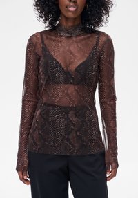 Brązowa przezroczysta bluzka z długim rękawem z wzorem węża, z wysokim kołnierzem i dopasowanym krojem. Pod spodem przez tkaninę widoczny jest czarny biustonosz.