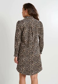 Vestido de leopardo con mangas largas, tejido suave, cuello alto y un leve vuelo. Presenta un detalle de espalda fruncida y un dobladillo redondeado.